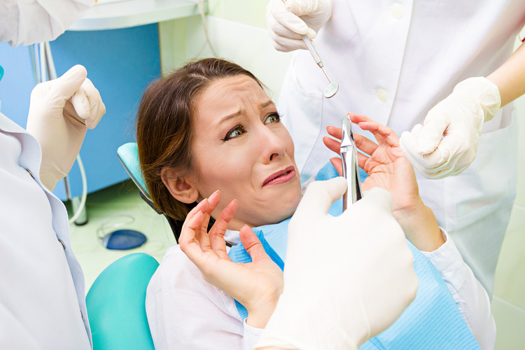 Closeup portrait young terrified girl woman scared at dentist visit, siting in chair, funny looking with fear, doesn't want dental procedure drilling tooth extraction isolated clinic office background